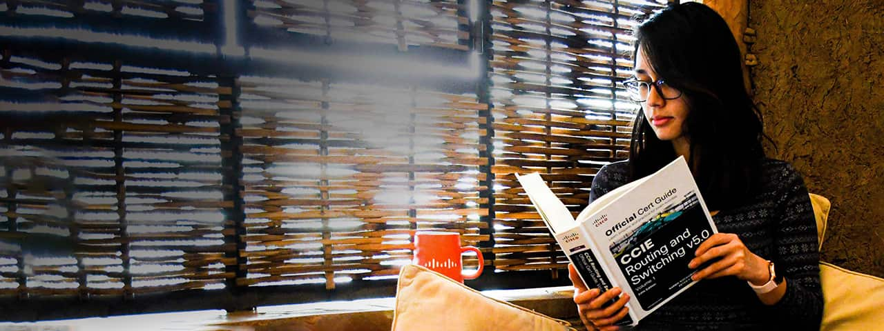 Female sitting criss-cross on a couch looking down at a Cisco Certification Guide Book