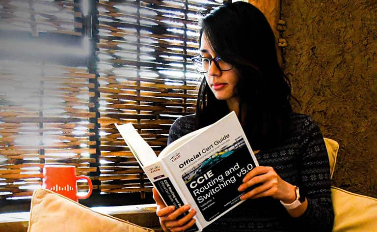 Female sitting criss-cross on a couch looking down at a Cisco Certification Guide Book